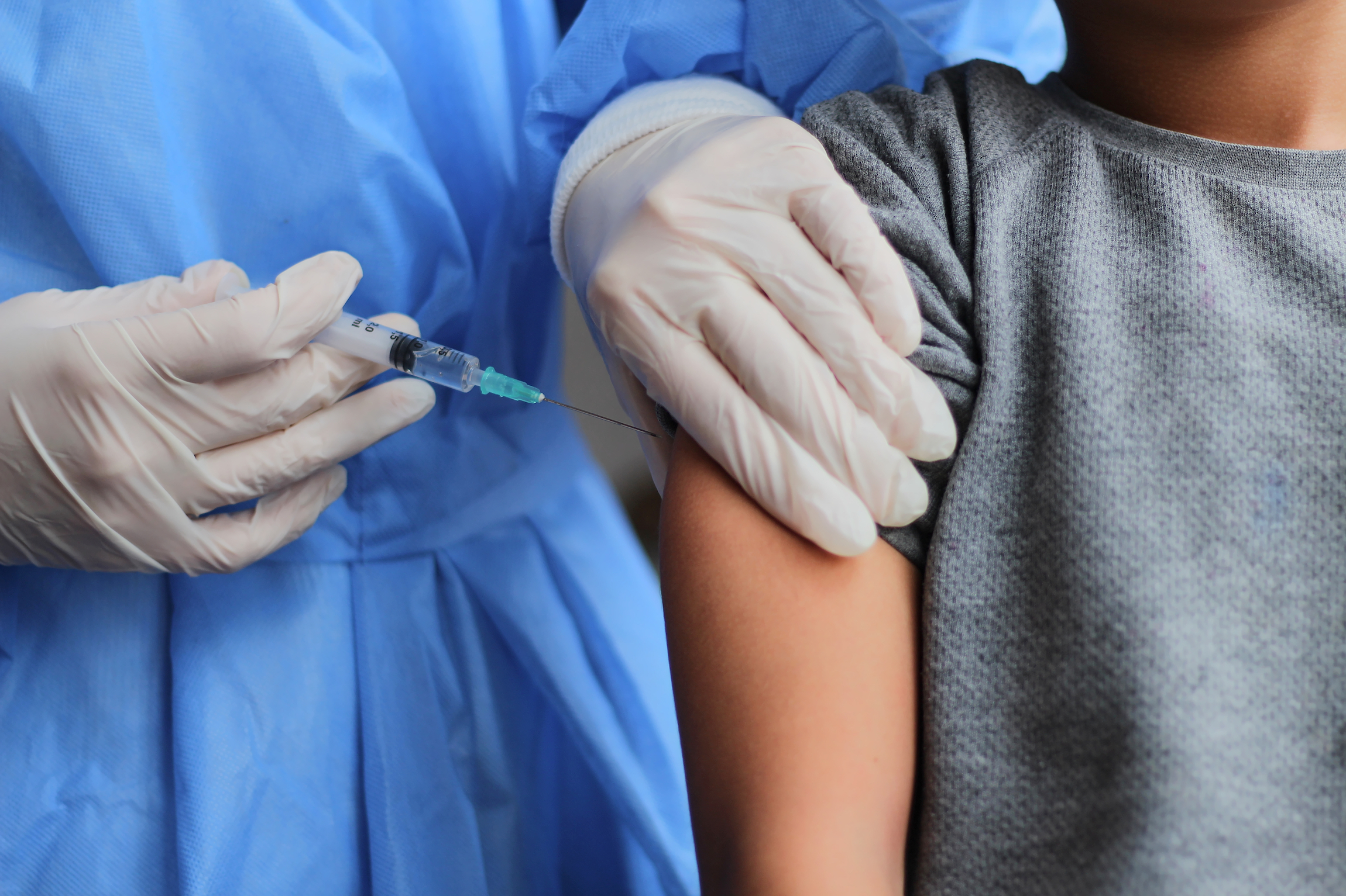 Mały chłopiec zaszczepiony z Covid-19. Dłoń młodego doctota trzymającego strzykawkę ze szczepionką.