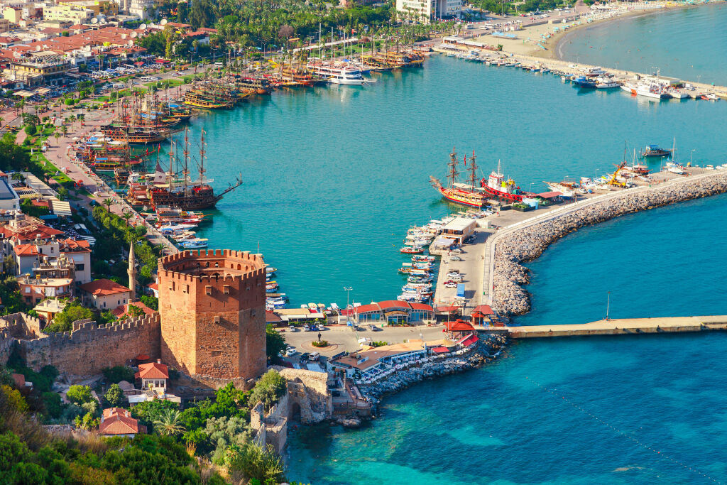 Krajobraz z przystani i wieży Kizil Kule na półwyspie Alanya, rejon Antalya, Turcja, Azja. Słynny cel turystyczny z wysokimi górami. Część starego zamku. Lato jasny dzień