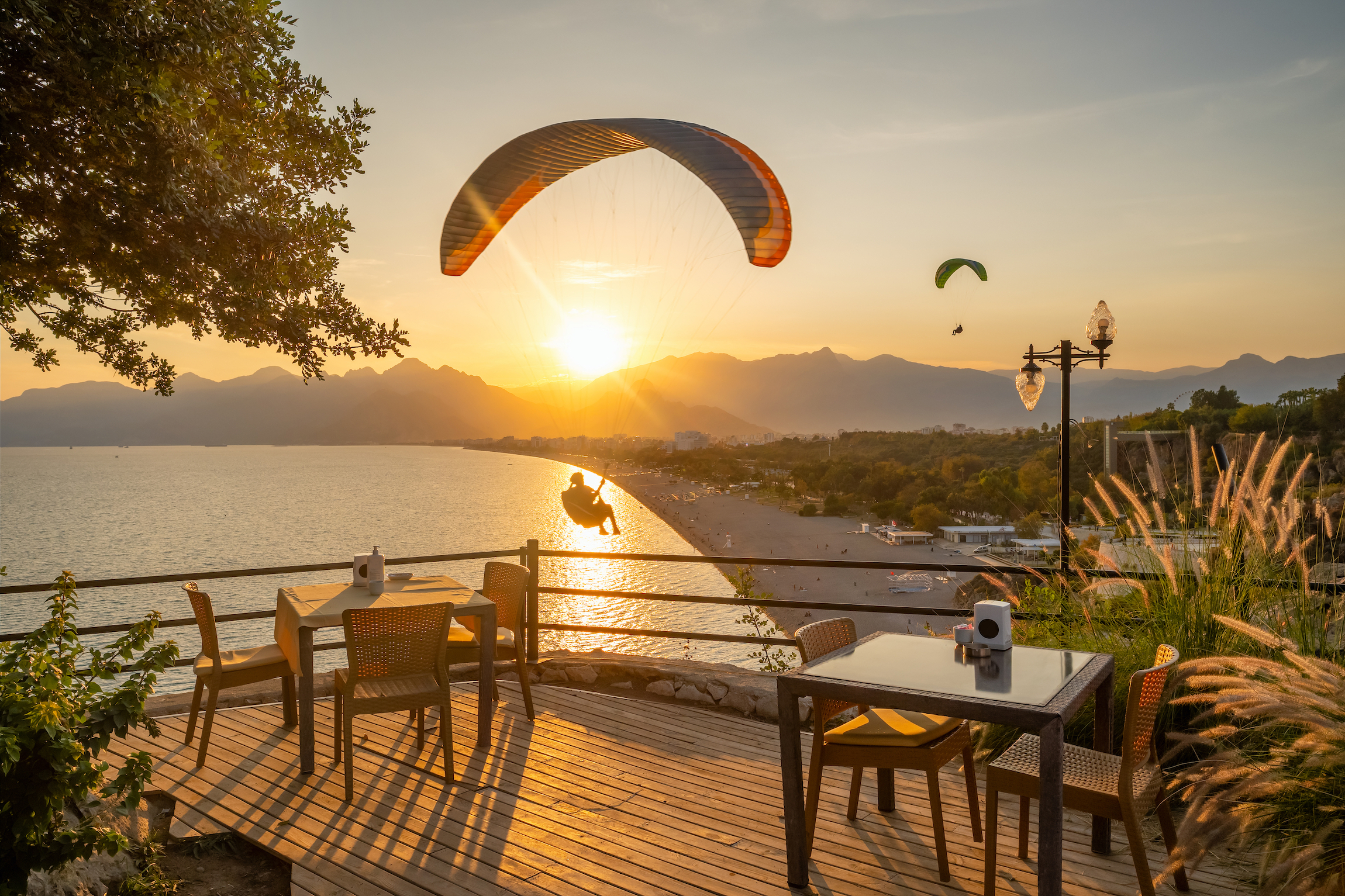 Paralotnia latająca nad plażą Konyaalti przy zachodzie słońca w Antalya, Turcja. Widok z zewnętrznej przytulnej restauracji w Antalyi